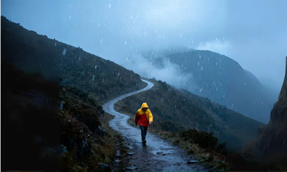 Persona usando casaca impermeable caminando bajo lluvia en ruta de montaña